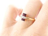 a woman ' s hand holding a ring with a red stone on it