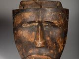 a close up of a wooden mask on a white surface