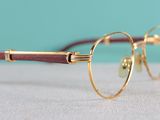 gold rimmed glasses with wooden temples on a white surface