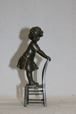 une statue représentant une petite fille assise sur une chaise