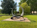 a sculpture in the middle of a grassy area with trees in the background