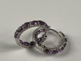 une paire de boucles d'oreilles créoles ornées de diamants violets et blancs, posées sur un fond blanc