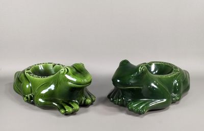 deux grenouilles en céramique verte assises l'une à côté de l'autre sur une surface blanche