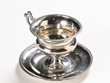 a silver cup and saucer sitting on a plate