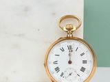 a gold pocket watch with roman numerals sitting on a marble block