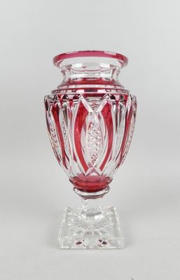 un vase en verre rouge posé sur un socle transparent, sur fond blanc