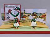 two figurines of people standing in front of a christmas card