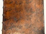 un vieux livre à la couverture marron posé sur une table blanche