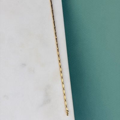 un collier en or avec une longue chaîne posé sur une dalle de marbre