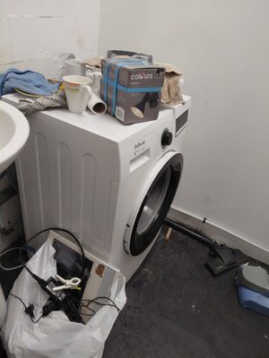 une machine à laver et un sèche-linge dans une salle de bains où se trouve un sac poubelle