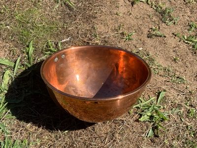 a copper bowl sitting on the ground in the grass