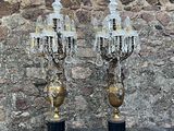 une paire de chandeliers en cristal et en laiton posés sur des socles devant un mur de pierre