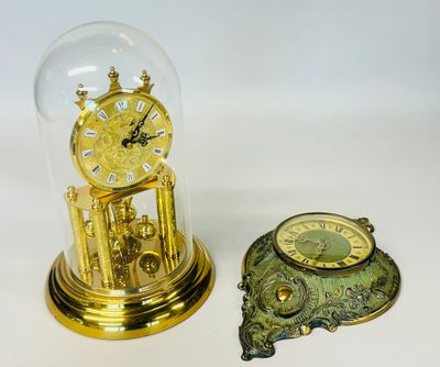deux horloges posées sur une table, sous un dôme en verre