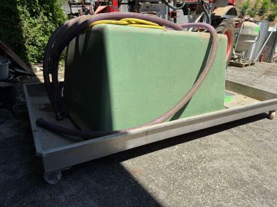 un conteneur vert posé sur un chariot, auquel est raccordé un tuyau