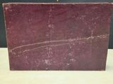 an old red book sitting on top of a table next to a black wall