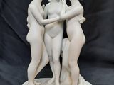 trois statues blanches représentant trois femmes se tenant par la main sur un fond noir