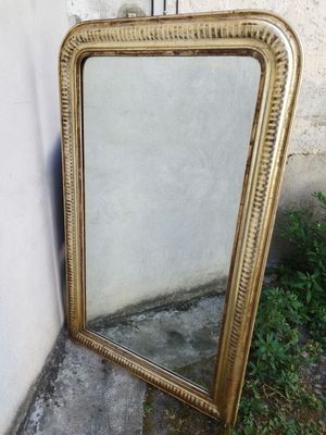 un miroir à cadre doré appuyé contre un mur, devant un mur blanc