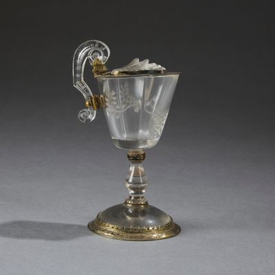 une coupe ancienne en argent et en verre, munie d'une anse, posée sur une surface grise