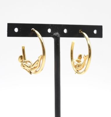 une paire de boucles d'oreilles créoles dorées posées sur un support en métal noir