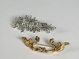 two pieces of gold and silver brooches on a white surface