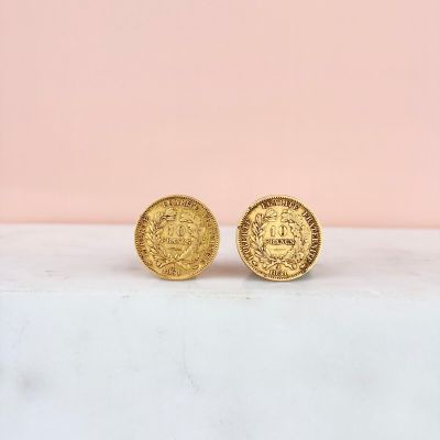 a pair of gold coin stud earrings sitting on top of a marble counter