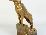 statue en laiton représentant un chien debout sur un rocher, avec un collier autour du cou