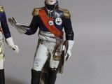 two figurines of two men dressed in military uniforms, one holding a sword and the other holding a bird