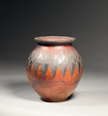 an orange and black vase sitting on top of a white table