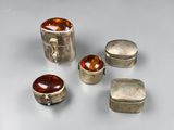 quatre bagues en argent et ambre et deux boîtes en argent posées sur un fond blanc