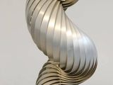 a metal spiral sculpture on a stand on a white surface