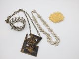 a close up of a necklace, bracelet, and brooch on a white surface