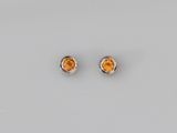 une paire de boucles d'oreilles en saphir orange posées sur une surface blanche