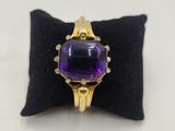 a close up of a ring with a purple stone on a black pillow