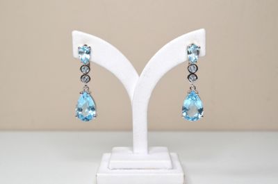 paire de boucles d'oreilles en cristal de topaze bleue et de topaze blanche, présentées sur un socle blanc
