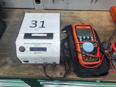 un multimètre orange et noir posé sur une table, à côté d'une boîte