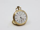 une petite montre de poche en or posée sur une surface blanche