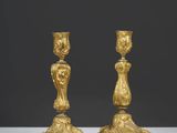 une paire de bougeoirs anciens en or posés sur une table blanche