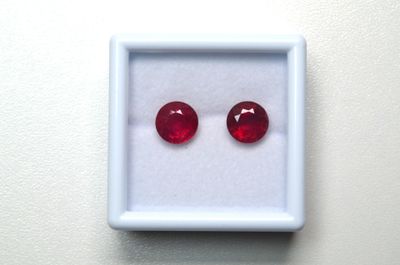une paire de rubis rouges dans un écrin blanc posé sur une surface blanche