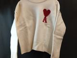 un pull blanc orné d'un cœur rouge, suspendu à un cintre