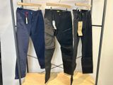 trois paires de pantalons suspendues à un portant dans un magasin