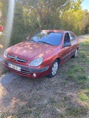 a red car parked in a field with trees in the background