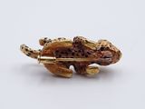 a gold brooch with a lizard on it on a white surface