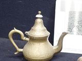 a gold teapot and a silver tea cup on a table