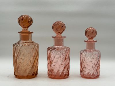 trois bouteilles en verre roses posées les unes à côté des autres sur une surface blanche