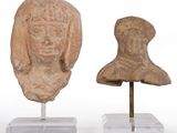 deux sculptures de têtes en argile posées sur des socles, disposées sur une surface blanche