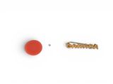 a red button and a gold pin on a white surface
