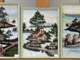 trois tableaux encadrés représentant des maisons et des bateaux, posés sur une étagère dans une pièce