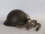 Un vieux casque est posé sur une surface blanche, entouré d'un ruban.