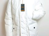 man wearing a white jacket and black pants standing against a white wall