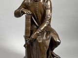 statue en bronze représentant un homme assis sur une chaise avec un chien